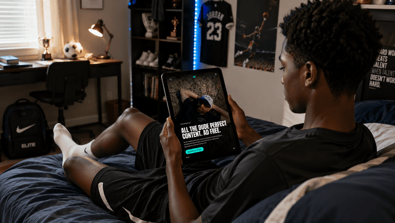 Teenage sports fan relaxing in his bedroom while exploring the Dude Perfect platform on a tablet.